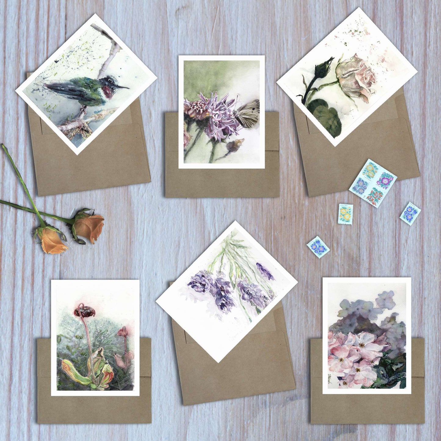Set of 6 assorted watercolor art greeting cards from the Violet Reverie collection fanned out on envelopes on wooden surface.