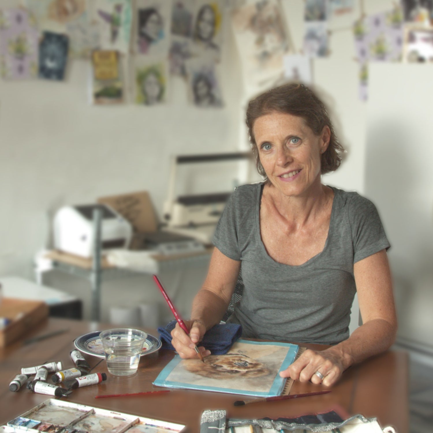 Artist Silvana Varriale painting a custom watercolor portrait of a poodle at her desk in her studio, original artwork hanging in the background | VARsee art