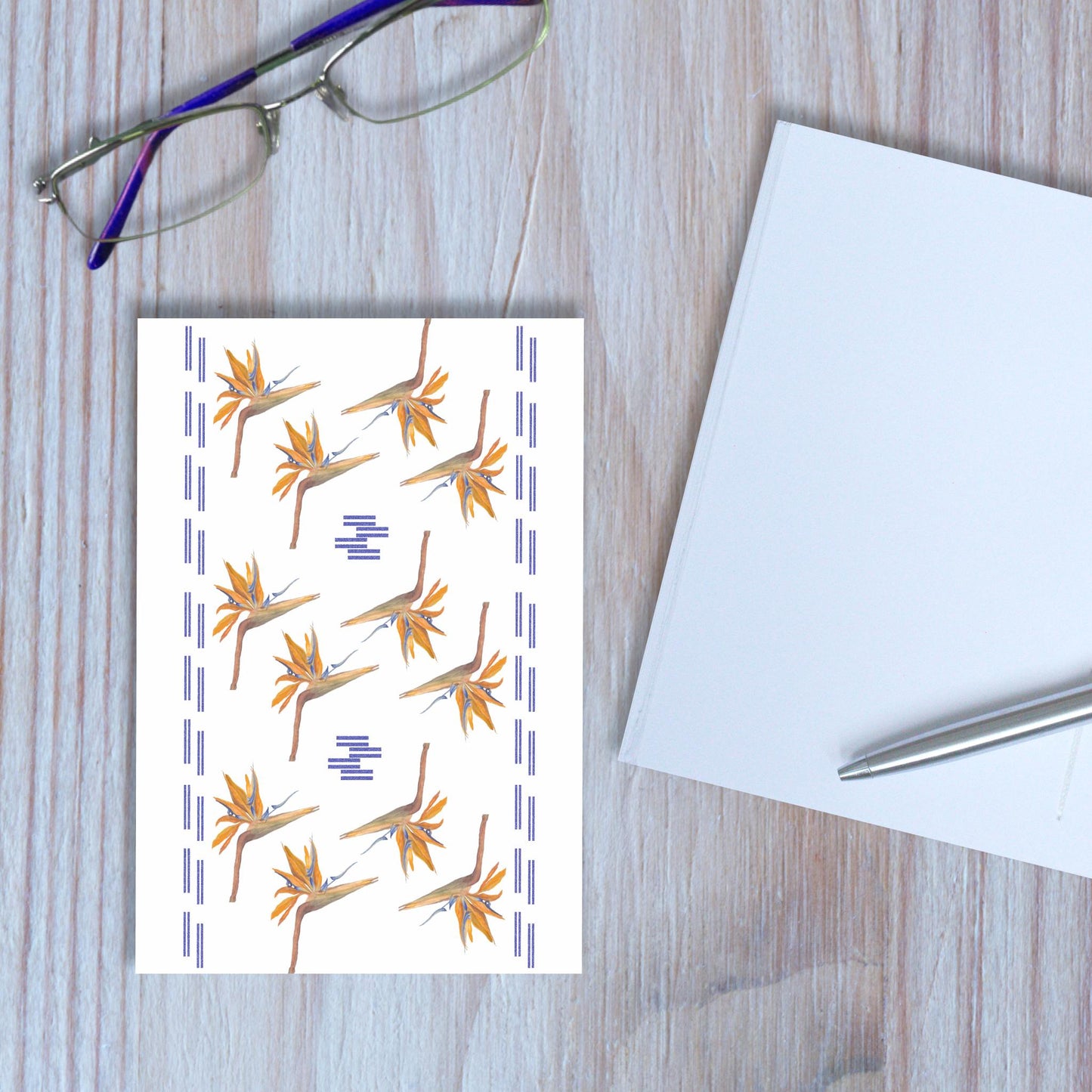 Bird of paradise flower design notebook closed, with another notebook open beside it, on wooden background.