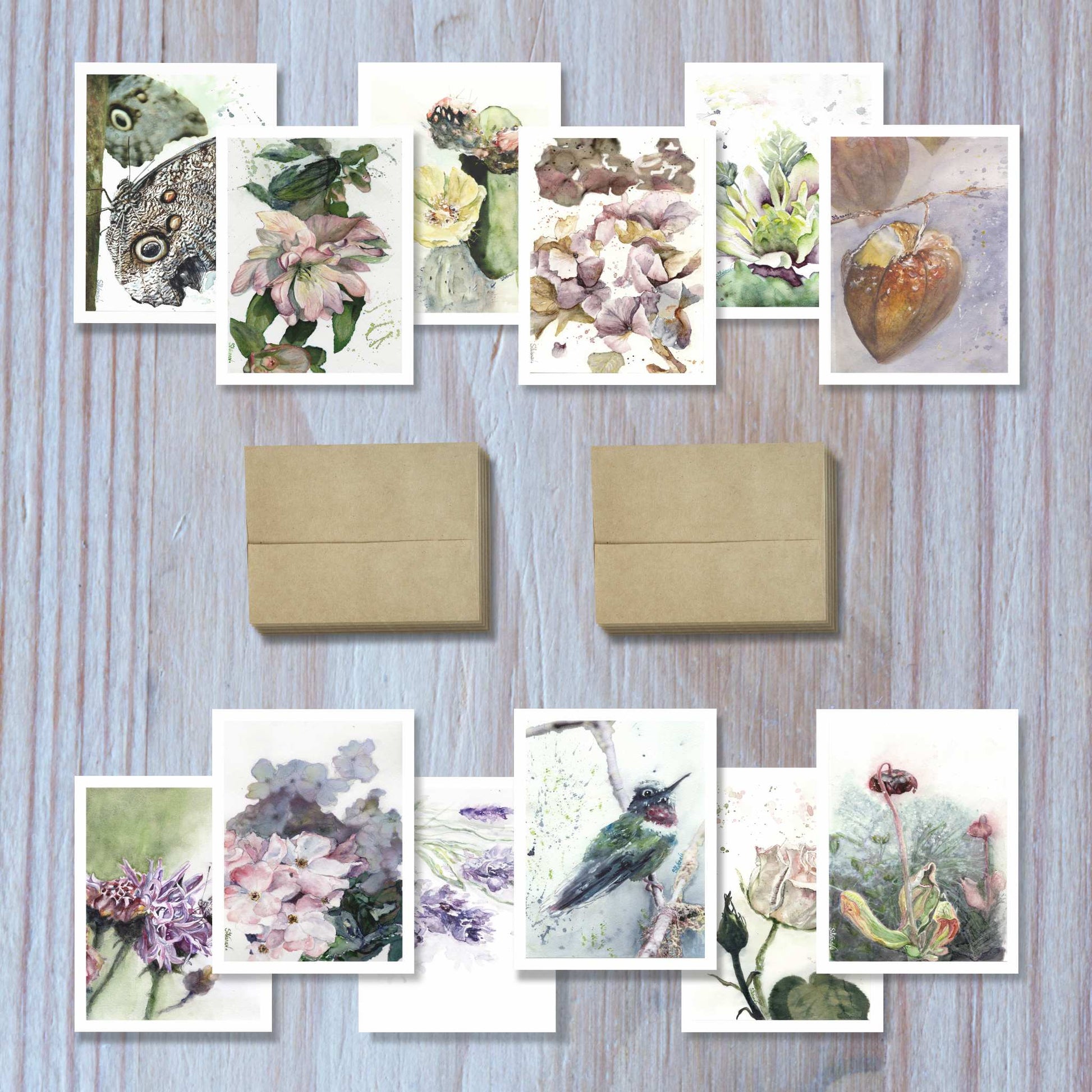 Set of 12 botanical watercolor greeting cards arranged in two rows of six with  envelopes on a table.