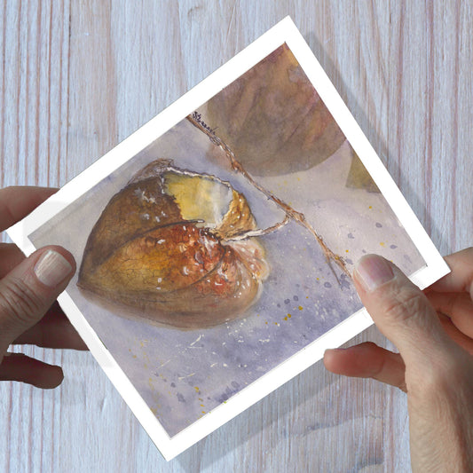 Hands holding a Chinese lantern watercolor greeting card, shown on a wooden surface