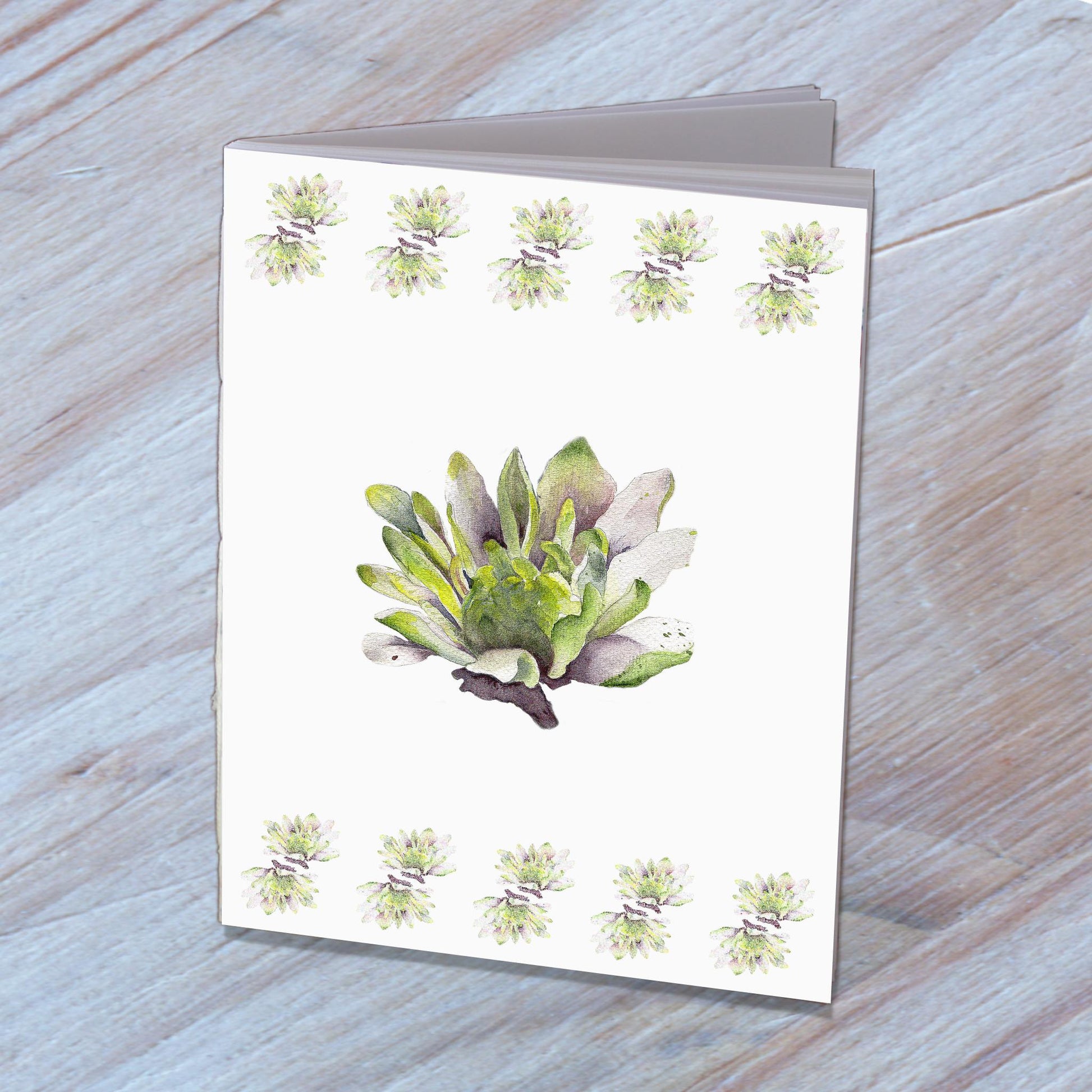 Handmade notebook with a cover designed from dahlia watercolor, standing on a wooden surface.