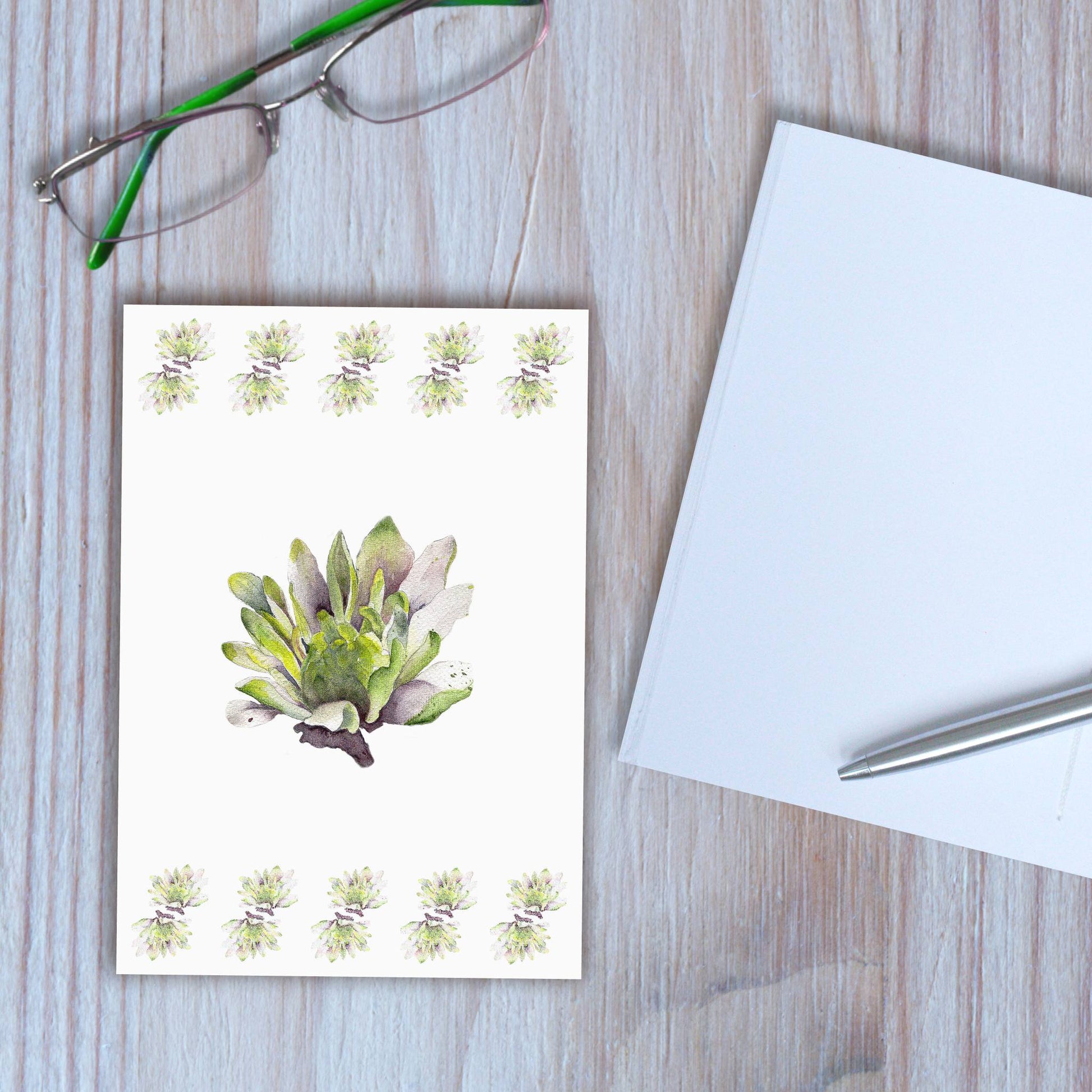 Dahlia design notebook closed, with another notebook open beside it, on wooden background.