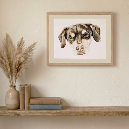 An original artwork print by Silvana Varriale for varsee, displayed in a light wood frame. The portrait is staged on a rustic wooden shelf with pampas grass and books, showcasing a warm, organic home decor aesthetic.