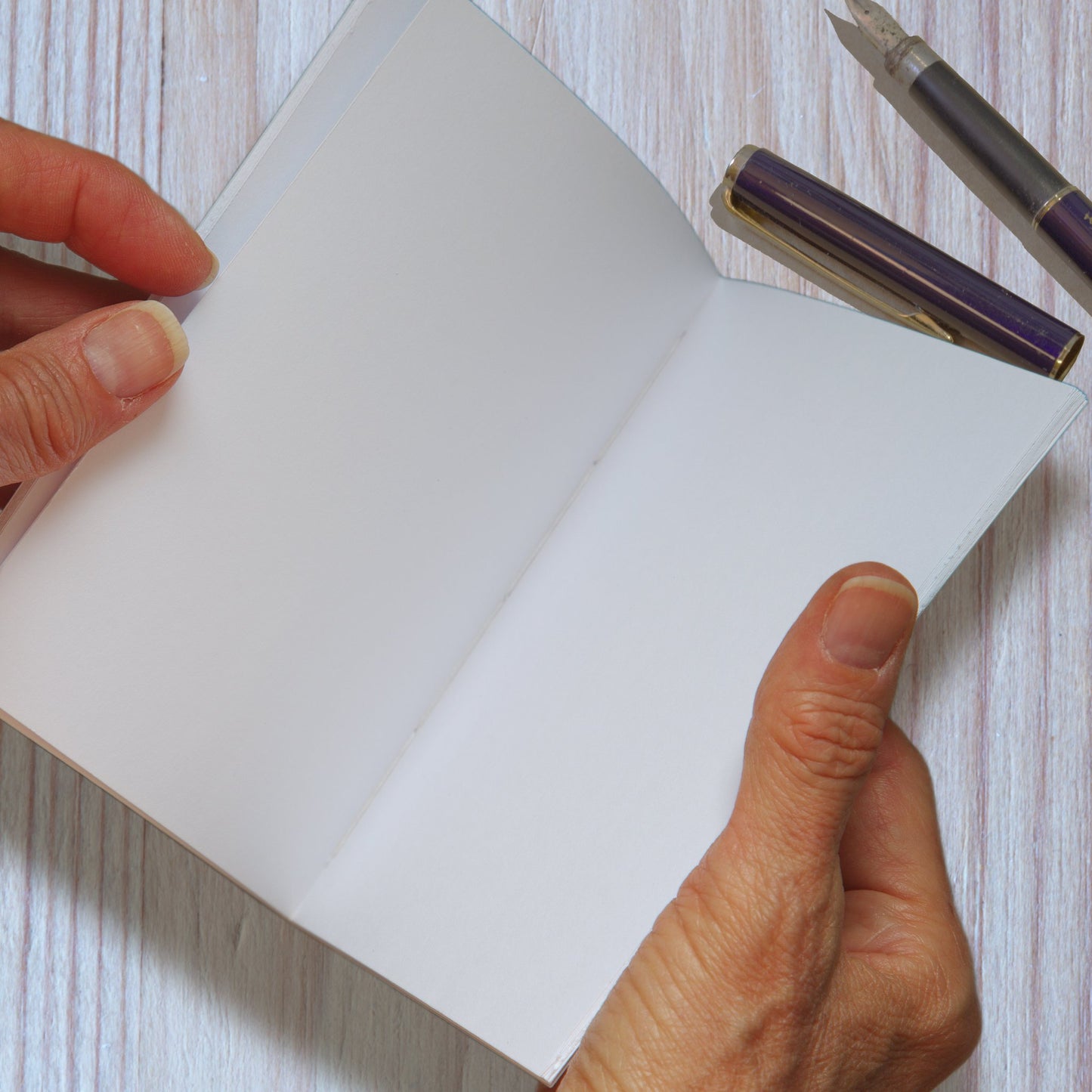 Hand-sewn handmade notebook open in hands, showing stitched binding and blank interior pages.