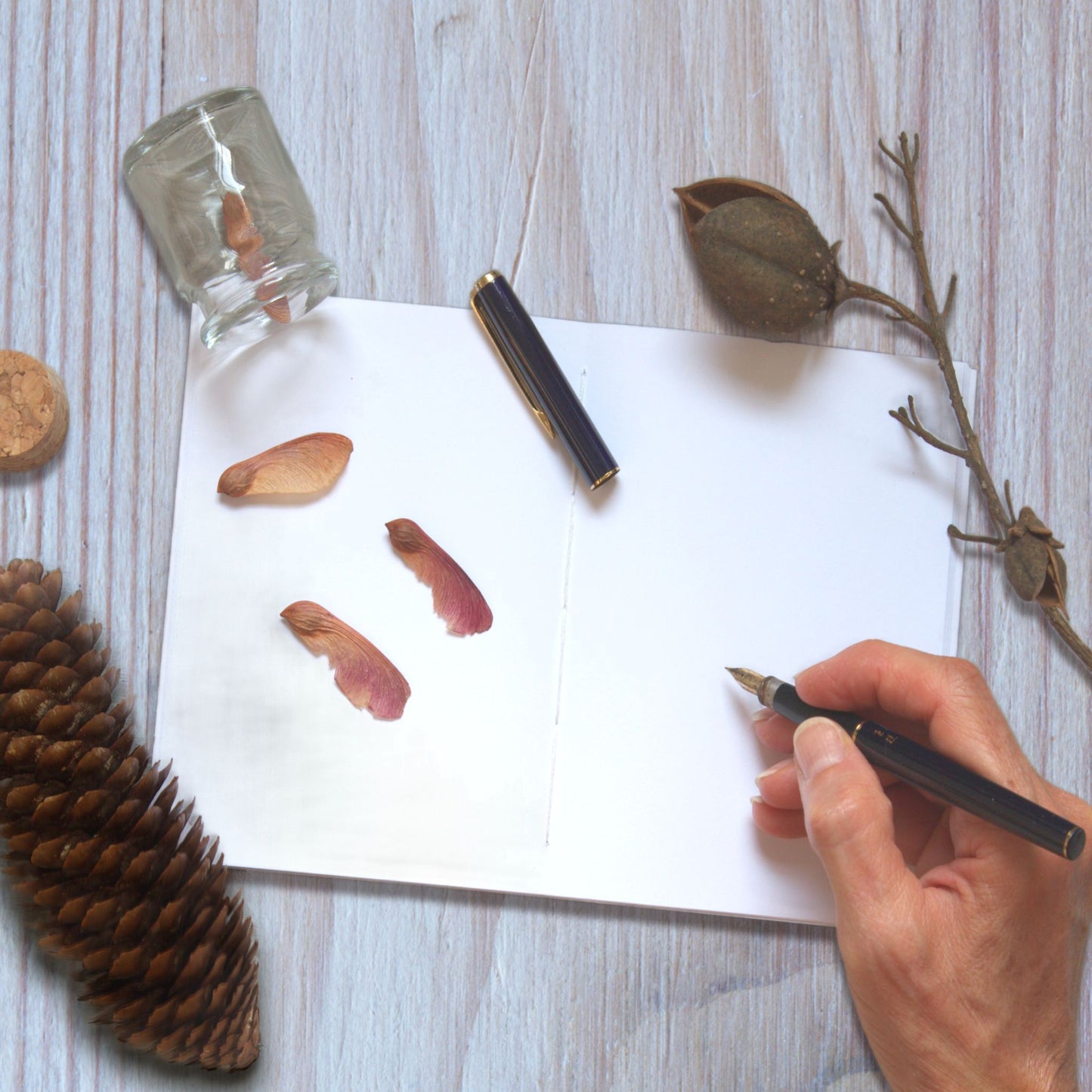 Writing by hand with a fountain pen in an open notebook on a wooden surface.
