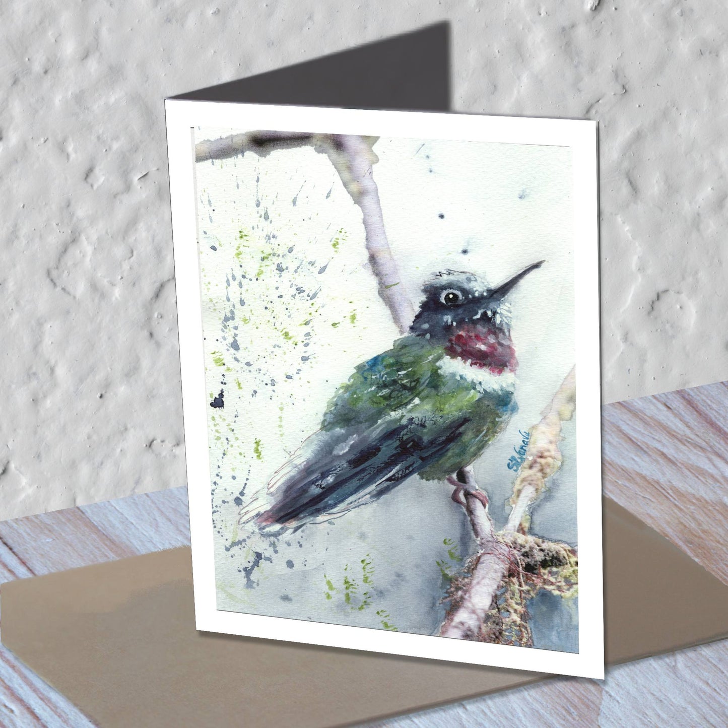 Hummingbird watercolor greeting card standing on a kraft envelope.