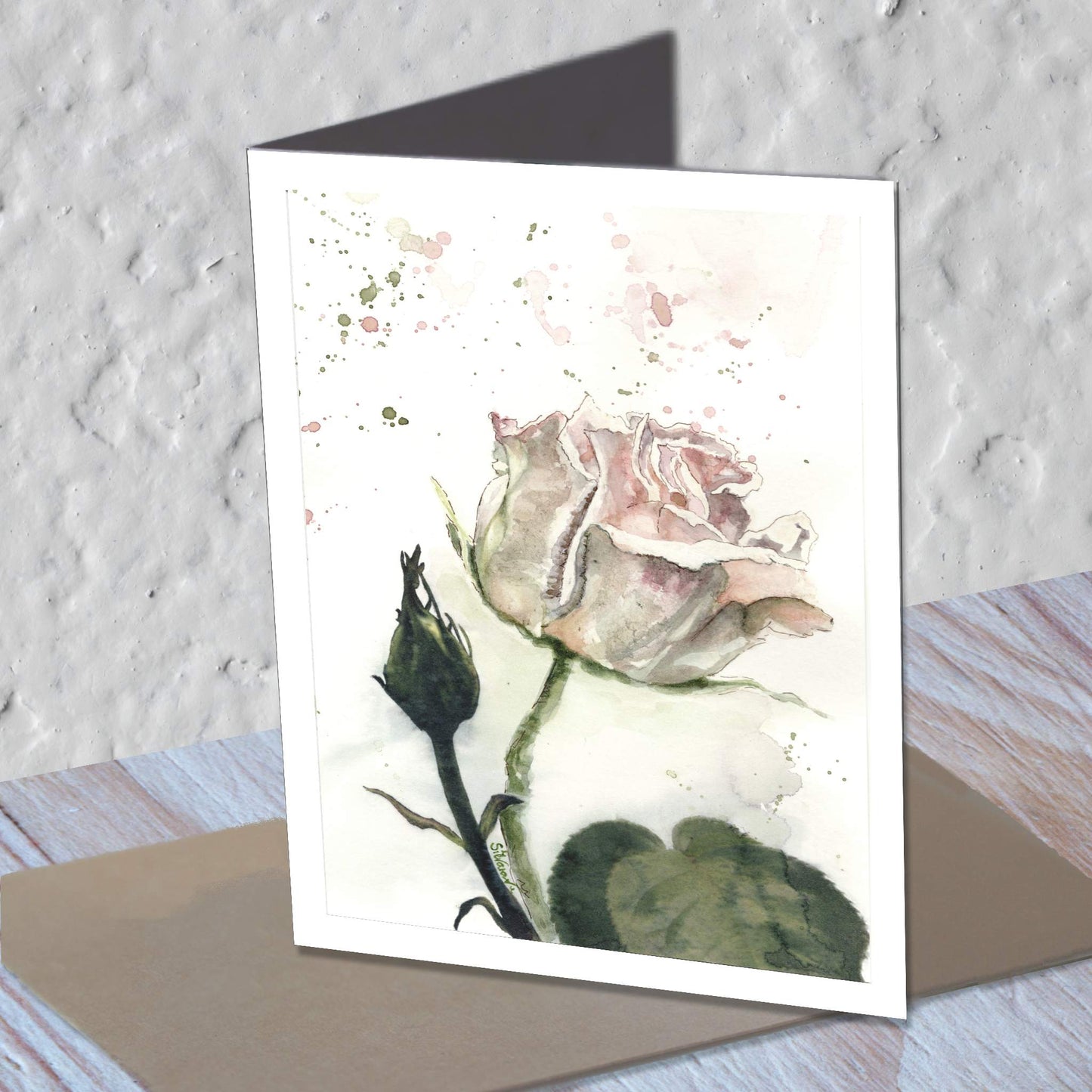 Pink rose watercolor greeting card standing on a kraft envelope.
