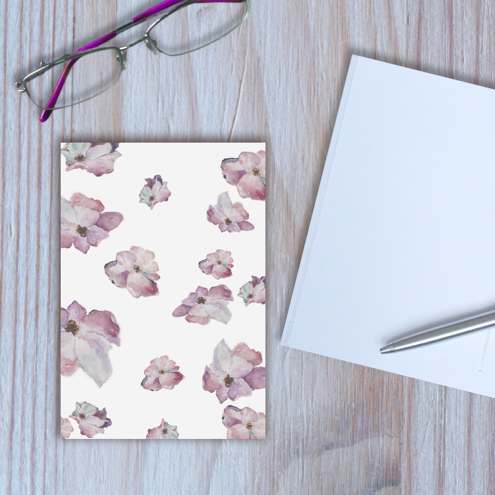 Wild roses design notebook closed, with another notebook open beside it, on wooden background.