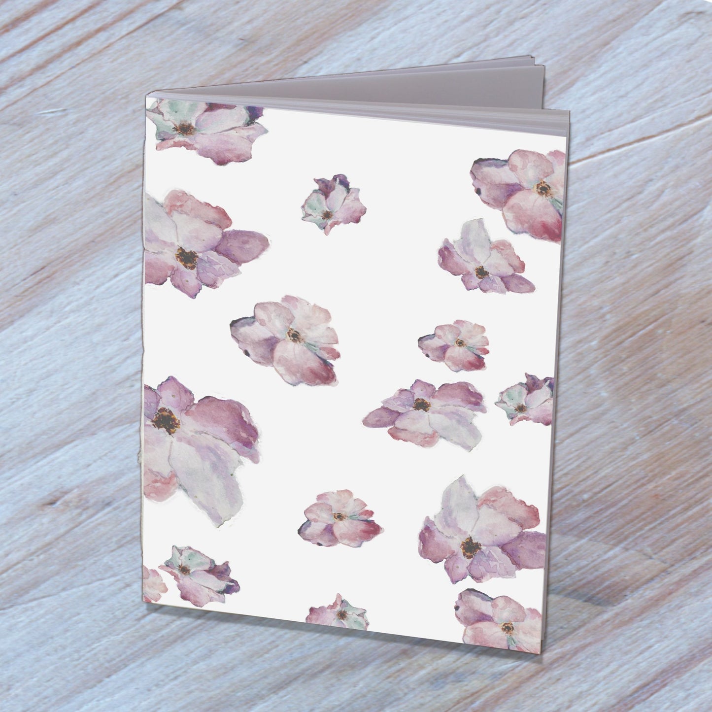 Handmade notebook with a cover designed from wild roses watercolor, standing on a wooden surface.