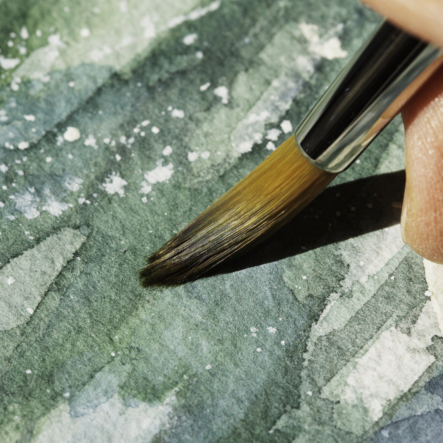Close up detail or the original watercolor "Wingspan airlines" by Silvana Varriale. Here a brush with brown bristles is layering green watercolor pigment on rough watercolor paper